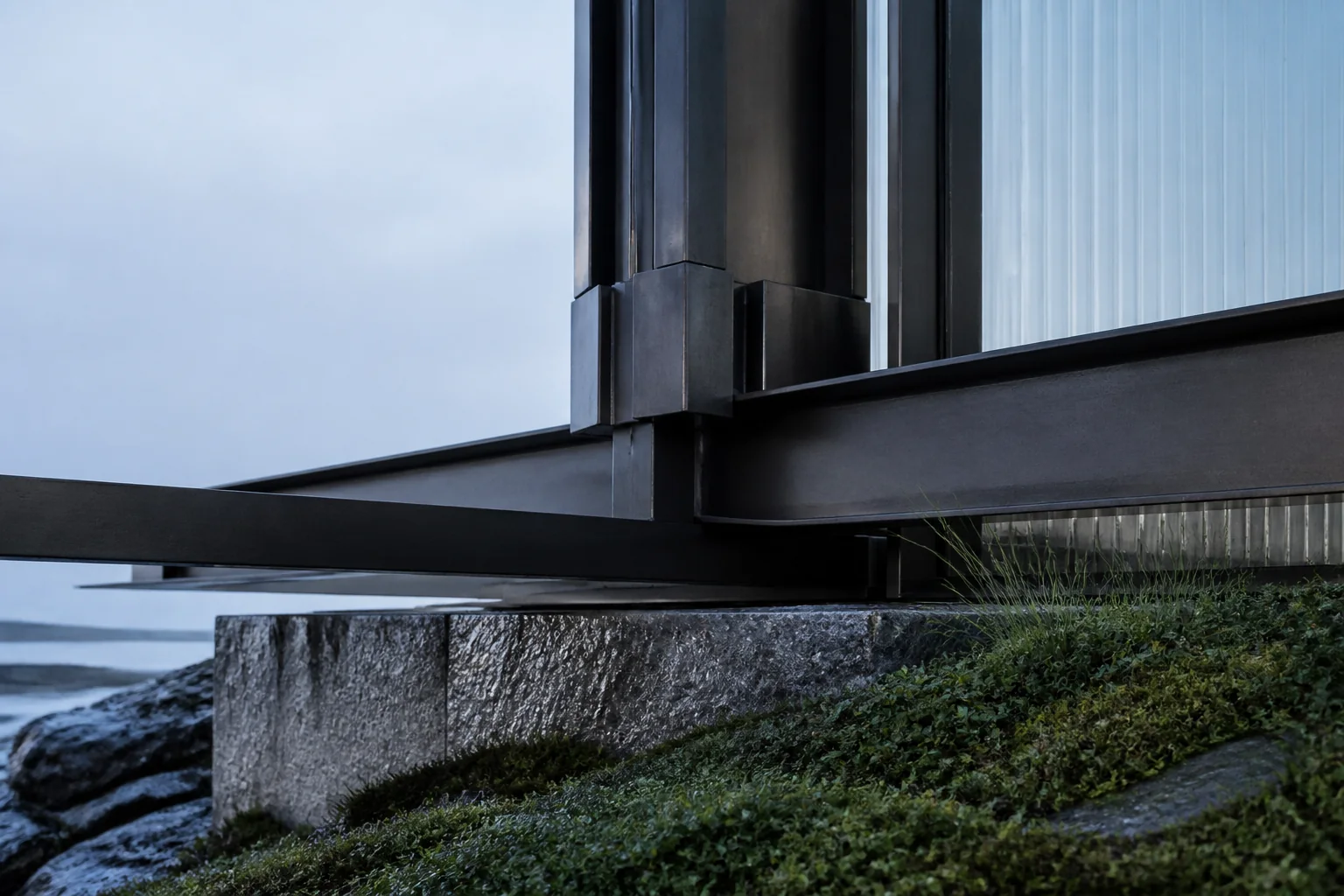 Steel beams meeting a stone foundation beside green groundcover